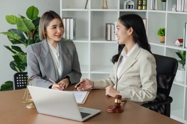 Bir kadın, masa başında dizüstü bilgisayarı ve sandalyesi olan bir belge imzalıyor. Kadın takım elbise giyiyor ve kalemle yazıyor. Sahne profesyonel bir ortam öneriyor.