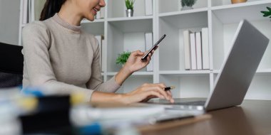 İş kadını laptopta çalışırken akıllı telefon kullanır, bilgisayarla aygıt arasındaki verileri senkronize eder, kurumsal aygıtlar ve iş uygulaması kullanır.