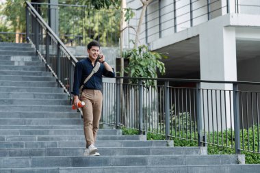 İş merkezinde cep telefonu ve çanta kullanarak yürüyen genç bir iş adamı..