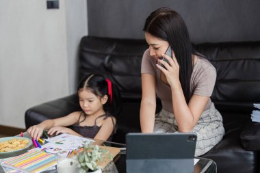 Evde çalışan bir iş adamı. Çalışan kadın cep telefonuyla konuşuyor, tablet üzerinde çalışıyor ve yaz boyunca kızına bakıyor..