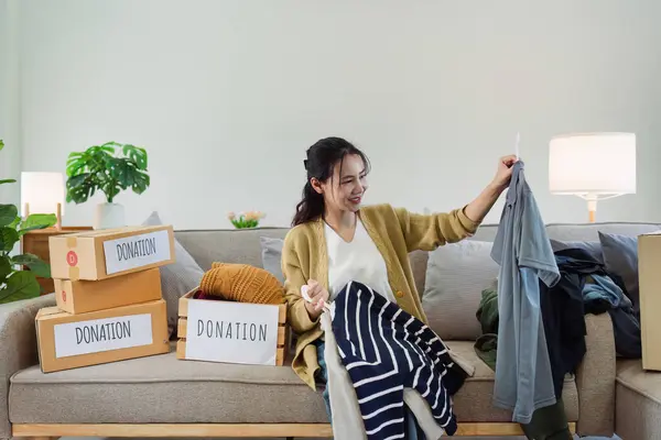 A woman is sorting through a pile of clothes and placing them in donation boxes. She is smiling as she works, indicating that she is happy to be helping others
