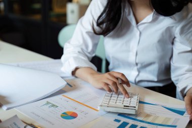 Bir şirketin mali belgelerindeki rakamları hesaplamak için hesap makinesi kullanan bir iş kadını, şirketin nasıl büyüyeceğini planlamak için tarihsel finansal verileri analiz ediyor. Mali konsept.