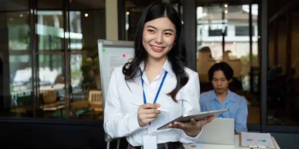 年轻的亚洲女企业家拿着数字平板电脑站在办公室里 企业女领导雇员 图库图片