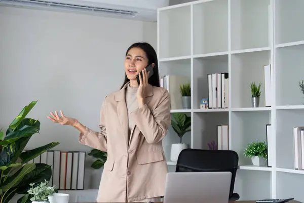与办公室里的客户通电话的女商人 用智能手机的年轻女人 办公室里使用移动电话的妇女的手 免版税图库照片