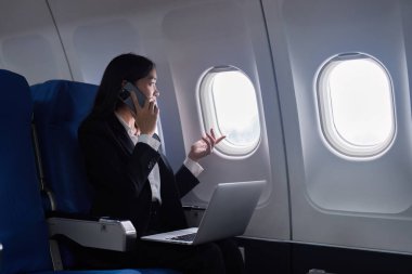 Uçakta dizüstü bilgisayar ve cep telefonuyla çalışan Asyalı güzel bir iş kadını. çalışma, seyahat, iş konsepti.