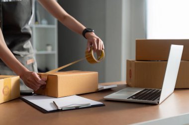 Genç girişimci bir kutuyu bantla mühürlüyor. Nakliyeye, paketlemeye, çevrimiçi satışa, e-ticaret konseptine hazırlık.