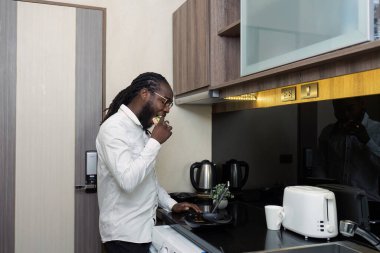 Afrikalı işadamı sabah sandviç yer ve şirket belgeleri üzerinde çalışmak için bir tablet kullanır. Evden çevrimiçi çalışırken.