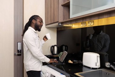 Afrikalı işadamı sabahları kahve içer ve şirket belgeleri üzerinde çalışmak için tablet kullanır. Evden çevrimiçi çalışırken.