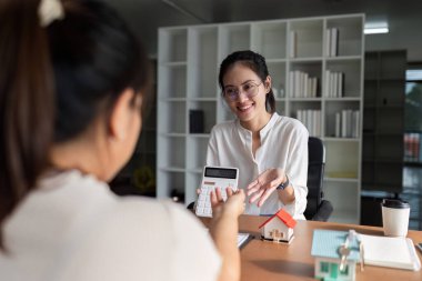 Emlakçı, alıcıların aylık ödemelerini hesaplıyor. Müşteri, konut ve sigorta veya kredi veya gayrimenkul satın alma sözleşmesini tartışıyor..