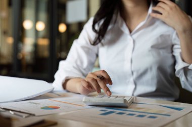 Bir şirketin mali belgelerindeki rakamları hesaplamak için hesap makinesi kullanan bir iş kadını, şirketin nasıl büyüyeceğini planlamak için tarihsel finansal verileri analiz ediyor. Mali konsept.