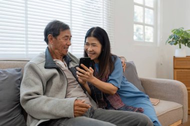 Mutlu evli çift akıllı telefon teknolojisi aygıtını kullanarak cep telefonuna bakıyor, kanepede dinleniyor ve online alışveriş yapıyor..