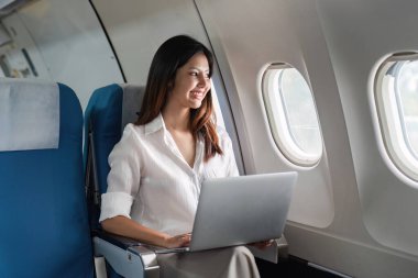 İşkadını birinci sınıf bir uçakta uçuyor ve çalışıyor, bir uçağın içinde dizüstü bilgisayar kullanarak oturuyor..