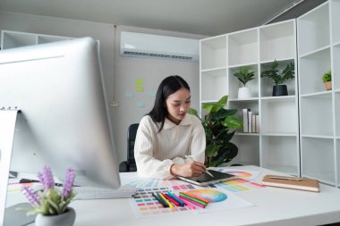 İş yerindeki tasarımcı grafik tablet ve renk paleti üzerine yeni bir proje çiziyor. Stüdyoda veya ofiste bilgisayar başında oturuyor..