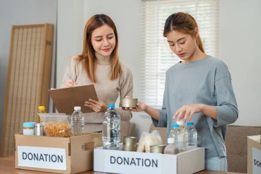 Hayır kurumları için kutularda yiyecek bağışları organize eden iki kadın, toplum desteğini ön plana çıkarıyor ve gönüllü olarak çabalıyor..