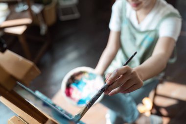 Tuvale fırça ve paletle resim yapan bir kişi, bir ev stüdyosunda hobi edinmenin neşesini ve yaratıcılığını sergiliyor..