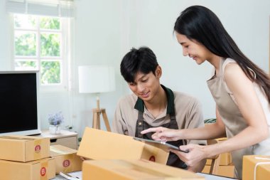 Genç girişimciler, modern bir iç işlerinde ambalaj ürünleri ile çevrili olan e-iş operasyonlarını yönetmek için dijital cihazlar kullanıyorlar..