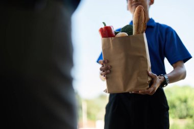 Bir teslimatçının, modern teslimat hizmetlerini sembolize eden bir poşet dolusu erzağı teslim edişi..