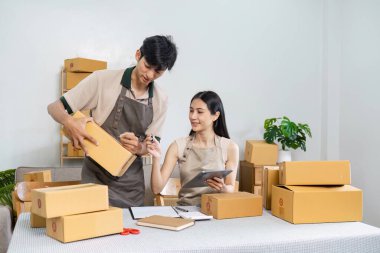Küçük işletmelerinde birlikte çalışan genç bir çift, kutuları paketliyor ve bir tablet kullanıyor, modern bir ev ofisinde takım çalışması ve girişimcilik sergiliyor..