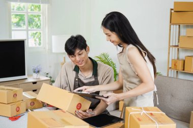 İki genç girişimci kutu paketliyor ve küçük bir işletme ofisinde envanter yönetiyor, takım çalışması ve modern e-ticaret operasyonları sergiliyorlar..