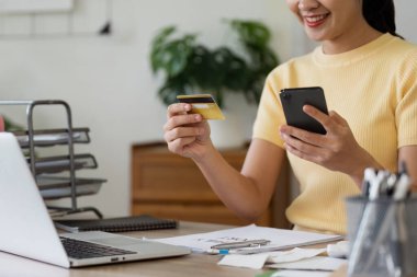 Günümüz dijital ödeme kolaylığını vurgulayarak, internet üzerinden alışveriş yapmak için kredi kartı ve akıllı telefon kullanan bir kadın.