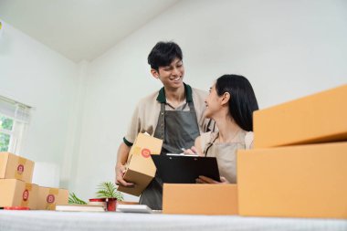 Ofislerinde birlikte çalışan bir çift online siparişler için kutuları paketliyor. Küçük işletmeleri, e-ticareti ve girişimciliği temsil eder.