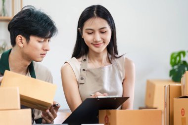 İki genç işletme sahibi modern bir küçük işletme ofisinde işbirliği yapıyor, nakliye kutuları ve evrak işlerini düzenliyorlar..