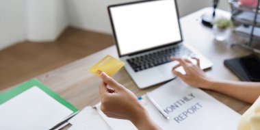 İnternet üzerinden alışveriş yaparken elinde kredi kartı tutan bir kadın. Aylık raporu ve ahşap bir masada belgeleri olan bir kadın..