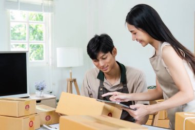 Genç girişimciler, modern bir iç işlerinde ambalaj ürünleri ile çevrili olan e-iş operasyonlarını yönetmek için dijital cihazlar kullanıyorlar..