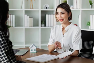 Ofiste bir müşteriye danışan kadın emlakçı, kapalı bir iş toplantısında profesyonel rehberlik ve müşteri hizmetleri sunuyor.