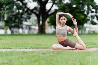 Parktaki pembe bir paspasın üzerinde yoga yapan genç bir kadın esneklik ve denge gösteriyor, sağlık ve sağlığı destekliyor..