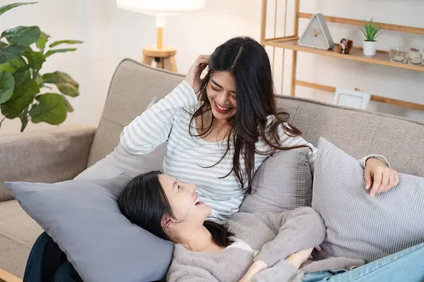 stock image Young smiling gay couple in casual wear spend time together while sitting on couch in cozy living room.