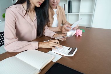 Genç bir çift hesap makinesi kullanarak masada oturuyor ve finansal belgeleri inceliyor, evde bütçelerini planlıyorlar..