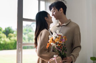 Genç bir çift pencerenin kenarında bir buket çiçek tutarak sevgi ve birlikteliği sembolize eden sıcak bir anı paylaşır..