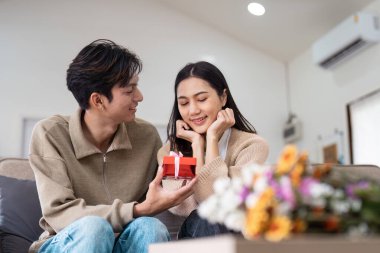 Mutlu bir çift evde özel bir anı paylaşıyor, hediyelerini paylaşıyor ve samimi, modern bir oturma odasında gülümsüyor..