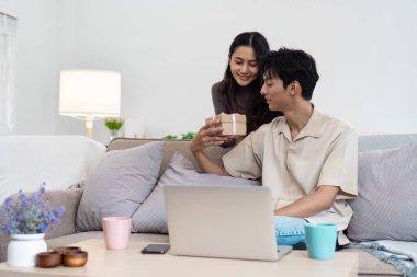 Evde özel bir anı paylaşan genç bir çift hediye alışverişinde bulunuyor ve sıcak bir oturma odasında birbirlerine eşlik ederek eğleniyorlar..