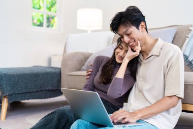 Mutlu bir çift oturma odalarında yerde oturuyor, birlikte dizüstü bilgisayar kullanıyorlar, modern ve rahat bir yaşam tarzı sergiliyorlar..