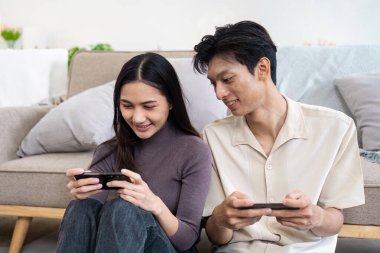 Yerde oturan mutlu bir çift, akıllı telefonları ve tabletleriyle meşgul, rahat ve modern bir yaşam tarzının keyfini çıkarıyorlar..