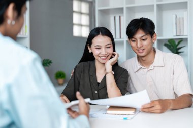 Genç bir çift, finansal planlamacıyla görüşür, belgeleri inceler ve modern ofis ortamında yatırım stratejilerini tartışır..