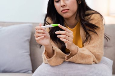 Kanepede oturan bir kadın, elinde hamilelik testi tutarken olumlu bir sonuç, sıcak bir yuva ortamında duyguları ve beklentileri yansıtıyor..