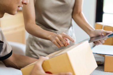 Küçük işletme sahipleri modern bir çalışma alanında sipariş ve envanteri karton kutularla yönetmek için dijital tablet kullanıyorlar..