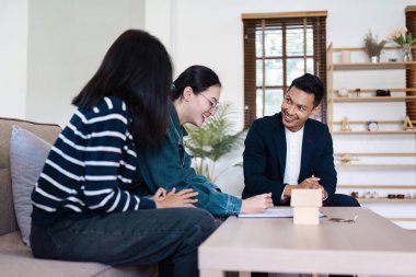 Bir emlakçı, müşteriye modern bir oturma odasında başarılı emlak işlemlerini ve ev sahipliğini sembolize eden yeni bir ev için sözleşme imzalamasında yardımcı olur..