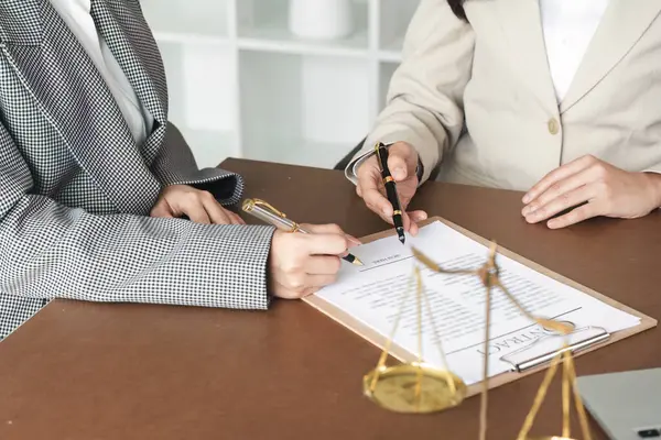 stock image Two lawyers reviewing and signing legal documents in a modern office setting, with scales of justice symbolizing fairness and law.