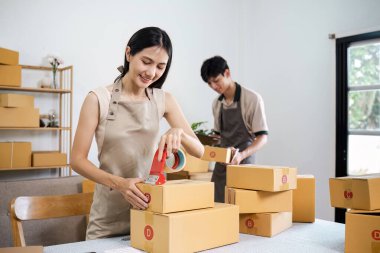 Modern bir ofis ortamında çevrimiçi küçük işleri için paketler hazırlayan iki genç girişimci.