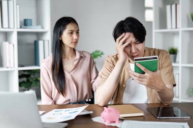 Masada oturan genç bir çift, mali planlama, tasarruf ve bankacılık tartışırken stresli görünüyorlar. Belgeler ve domuz kumbarası görünüyor..