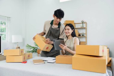 Çevrimiçi küçük işletmelerinde çalışan iki genç girişimci, bir tablet kullanıyor ve bir ofis ortamında paketler hazırlıyorlar..