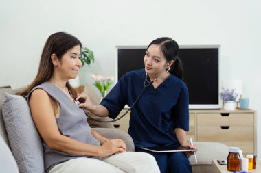 Bir hemşire evde yaşlı bir kadına steteskop kullanarak sağlık kontrolü yapıyor. Yaşlı hastalar için ev sağlığı hizmetleri.