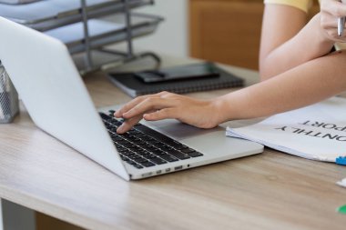 Evrak ve hesap makinesiyle çevrili bir ofis masasında dizüstü bilgisayar kullanarak faturaları ödeyen bir kişi..