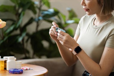 Evde çeşitli ilaç ve haplar düzenleyen, şişelerle sağlık ve ilaç yönetimini vurgulayan ve ahşap bir masa üzerinde su toplayan bir kadın.