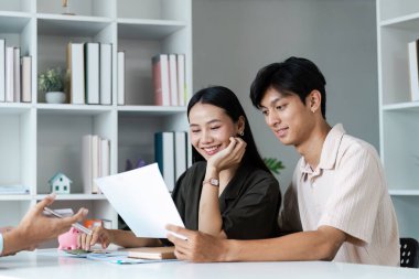 Neşeli bir çift masada oturup finansal belgeleri gözden geçirir ve geleceklerini modern bir ev ortamında planlarlar..