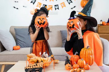 Cadılar Bayramı kostümü giymiş bir anne ve kız balkabağı süslemelerinin ve ziyafet salonundaki ziyafetin tadını çıkarıyorlar..